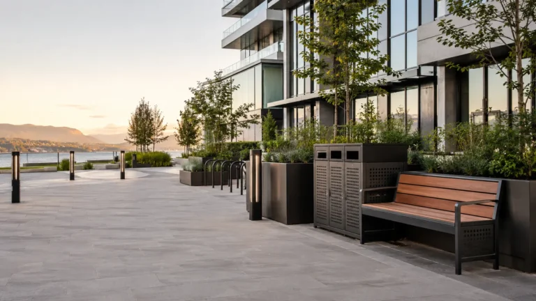 Metal benches, planters, waste enclosures and bike racks along a landscaped waterfront walkway