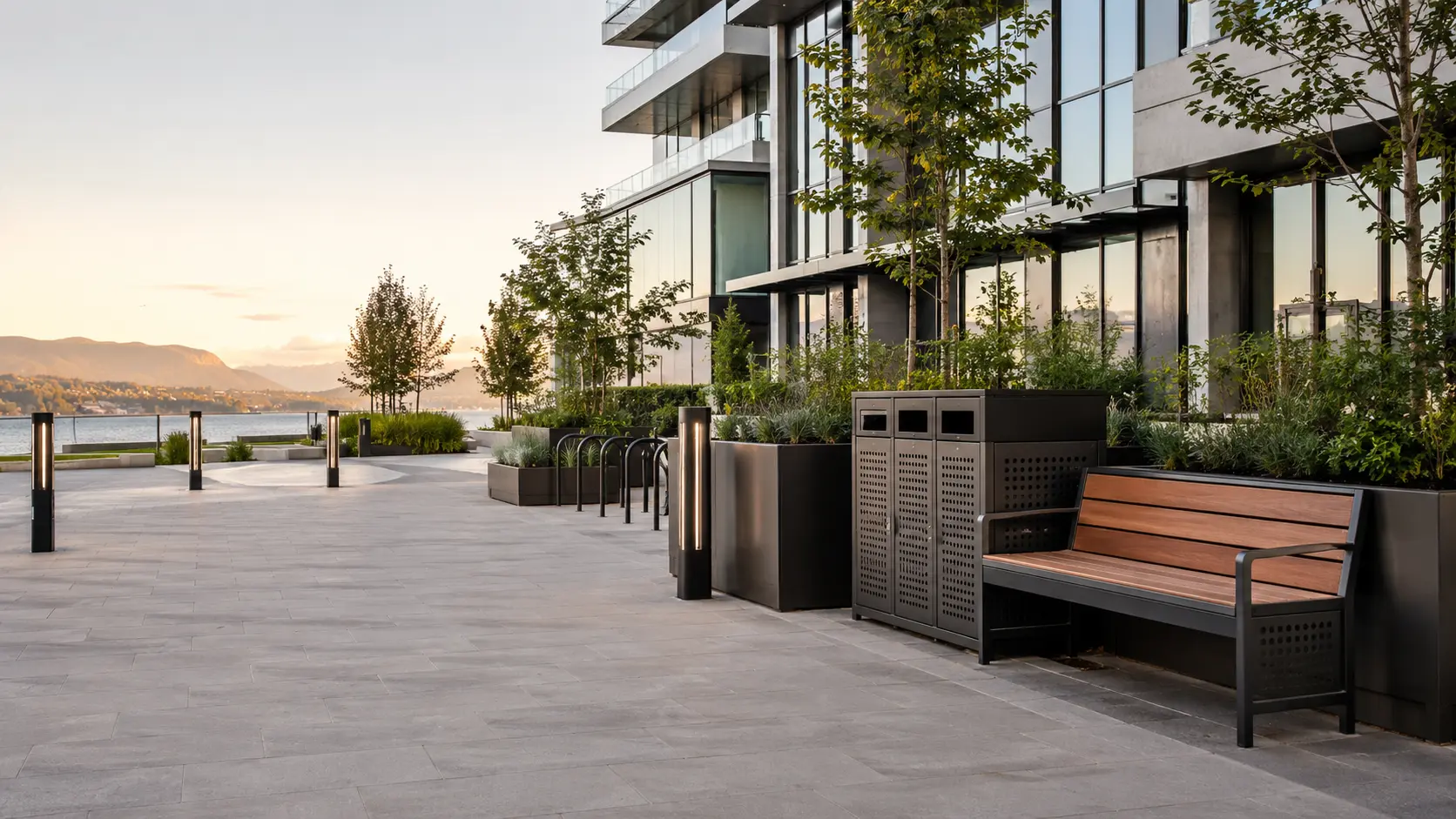 Metal benches, planters, waste enclosures and bike racks along a landscaped waterfront walkway