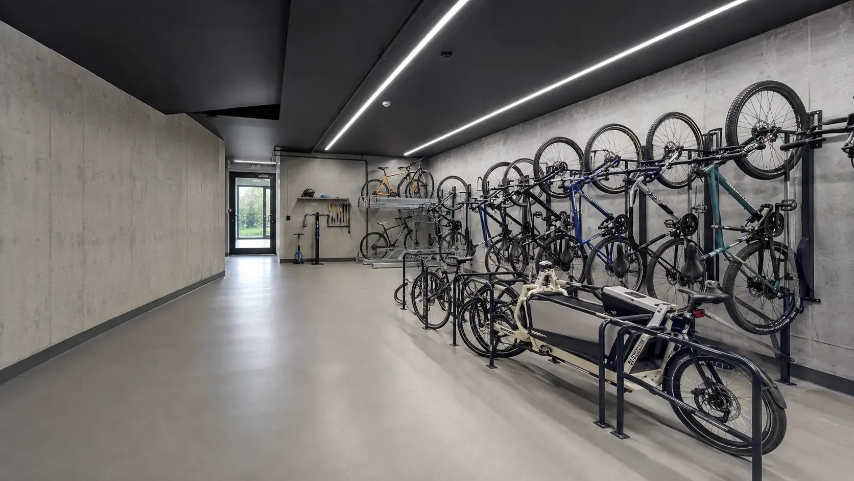Secure bike room with wall-mounted and floor bike racks along a concrete corridor