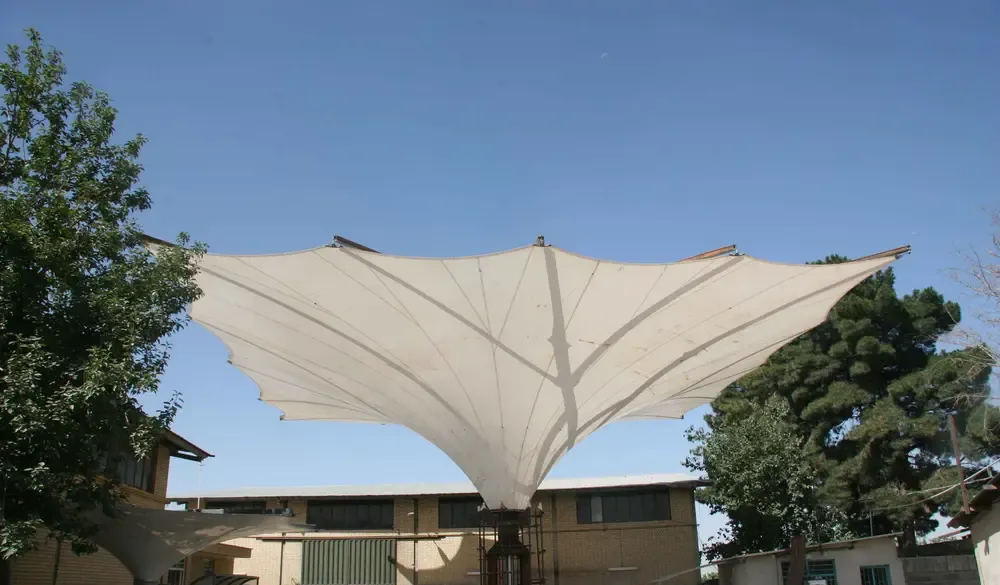 Large deployable shade umbrella with the tensioned fabric canopy fully open on its steel mast
