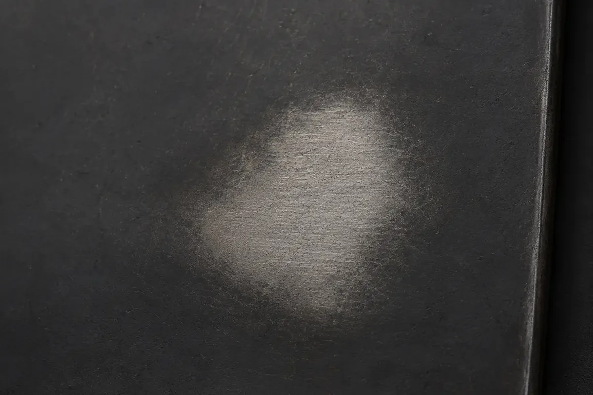 Blackened steel sample with a hand worn patch rubbed back to bare grey steel