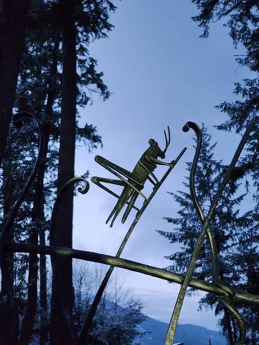 Forged grasshopper sculpture perched on a hand-forged branch bar