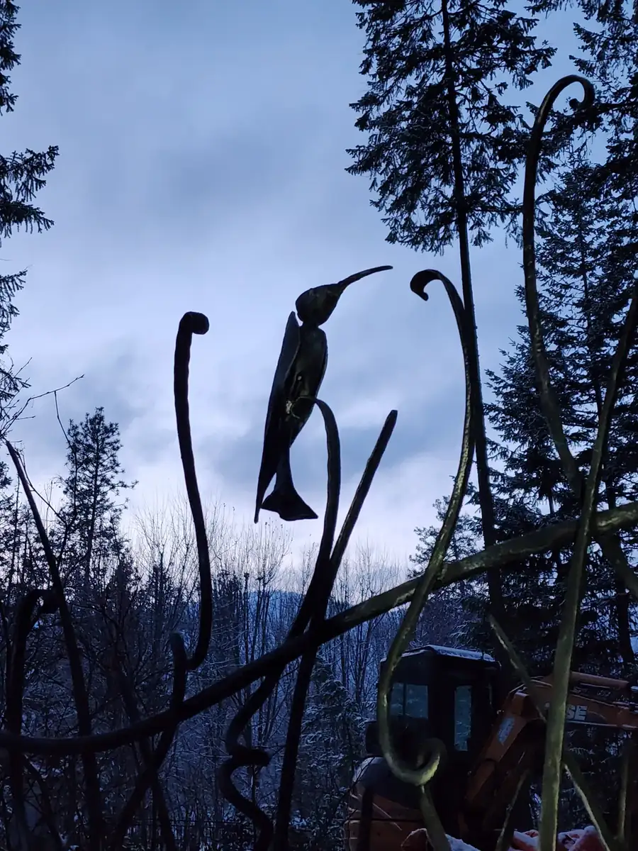Forged hummingbird sculpture set among curled tendrils on a wrought iron gate