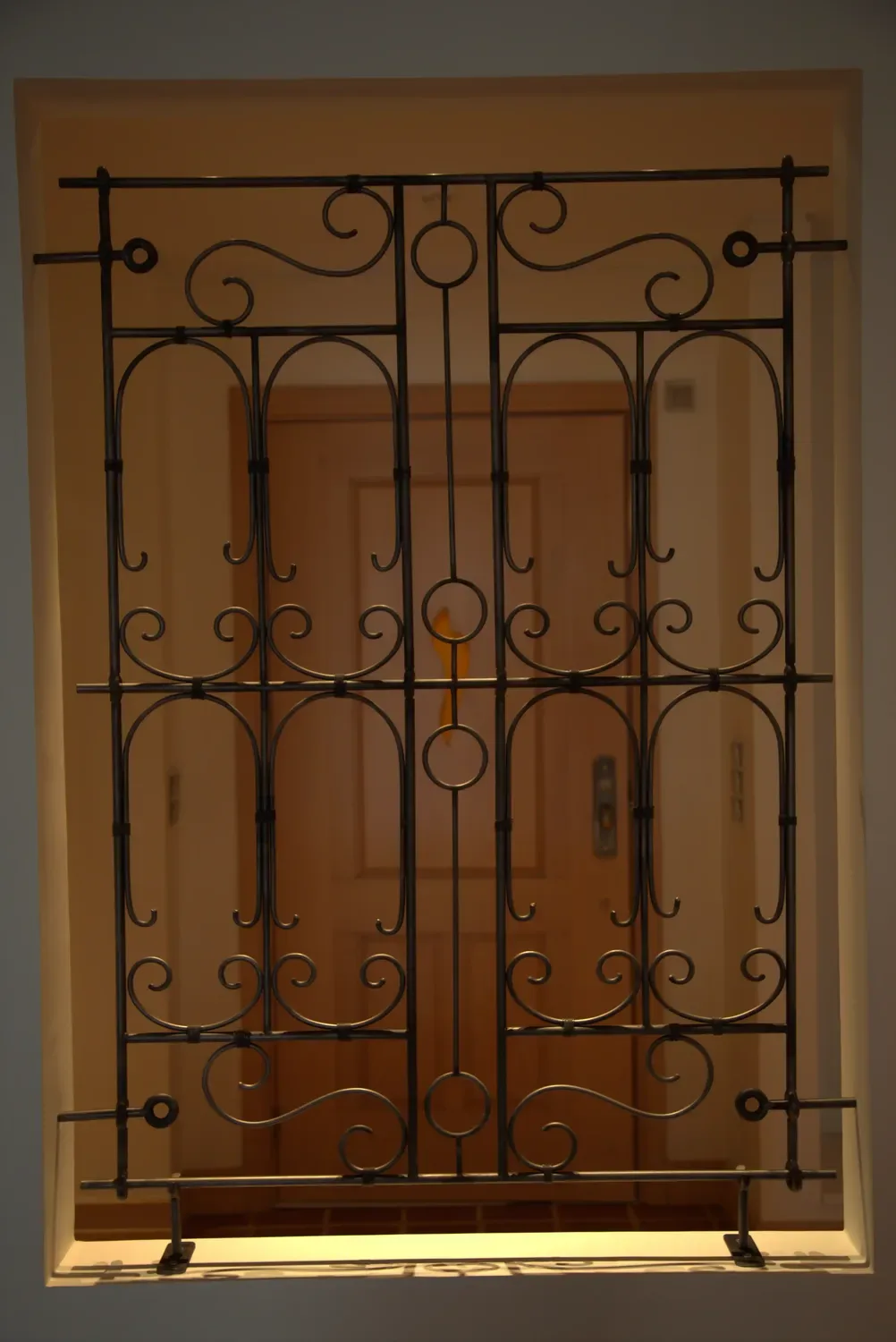 Forged decorative screen set into an interior wall opening, with scrollwork infill in a round bar grid