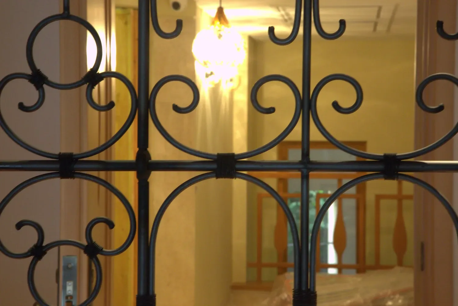 Detail of forged scrollwork in a screen, looking through to a lit corridor beyond