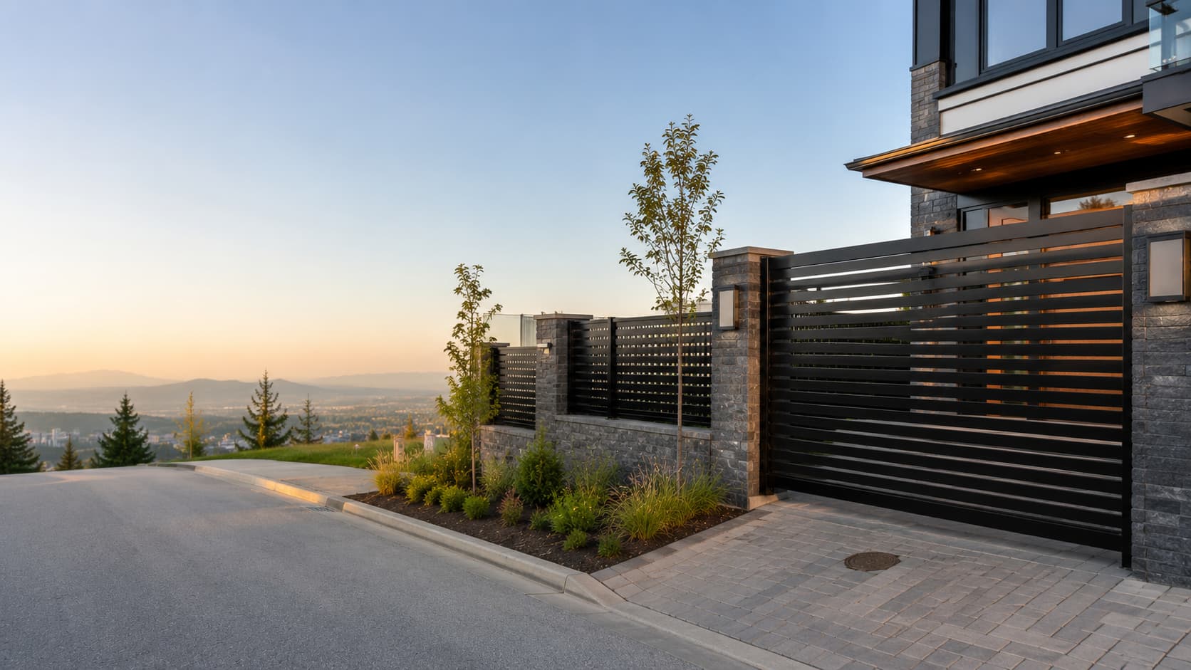 Black horizontal-slat steel driveway gate on dark stone piers at a Coquitlam hillside home, with the Fraser Valley and mountains beyond