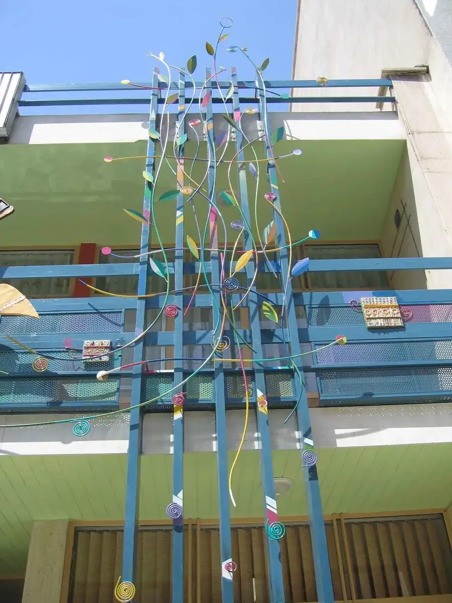 Tall assembly of steel stems rising through a balcony frame, with coloured leaf forms
