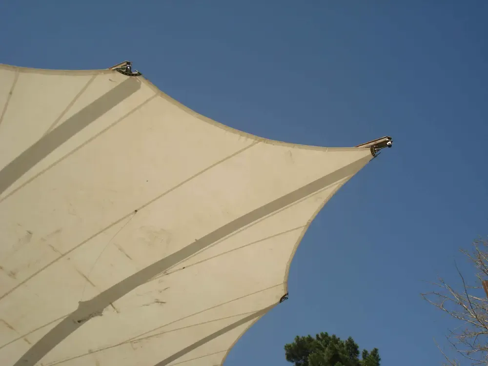 Detail of a steel arm tip and the reinforced edge of the fabric canopy against the sky